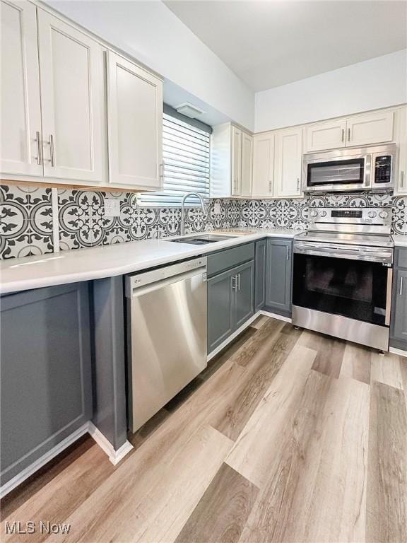 kitchen featuring appliances with stainless steel finishes, tasteful backsplash, sink, light hardwood / wood-style flooring, and gray cabinets