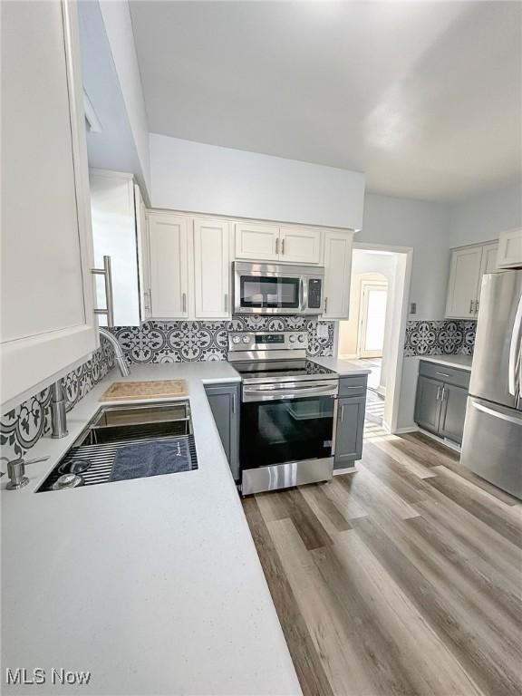 kitchen featuring white cabinets, appliances with stainless steel finishes, gray cabinets, and dark wood-type flooring