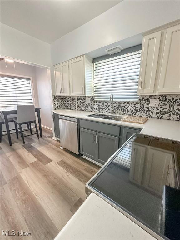 kitchen with backsplash, stainless steel dishwasher, gray cabinetry, sink, and light hardwood / wood-style flooring