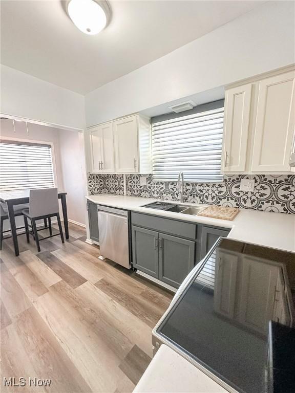 kitchen featuring light wood-type flooring, backsplash, gray cabinetry, sink, and dishwasher