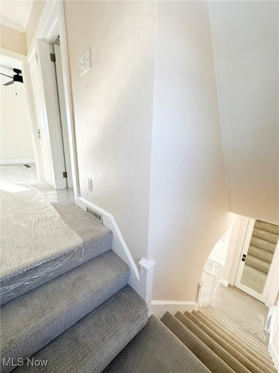 stairs featuring ceiling fan and ornamental molding