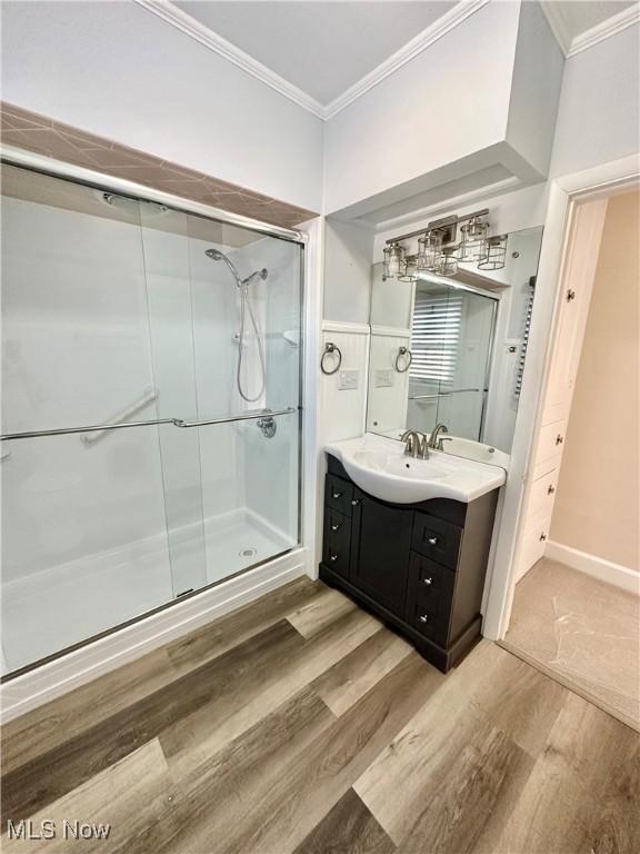 bathroom featuring vanity, hardwood / wood-style flooring, a shower with door, and crown molding