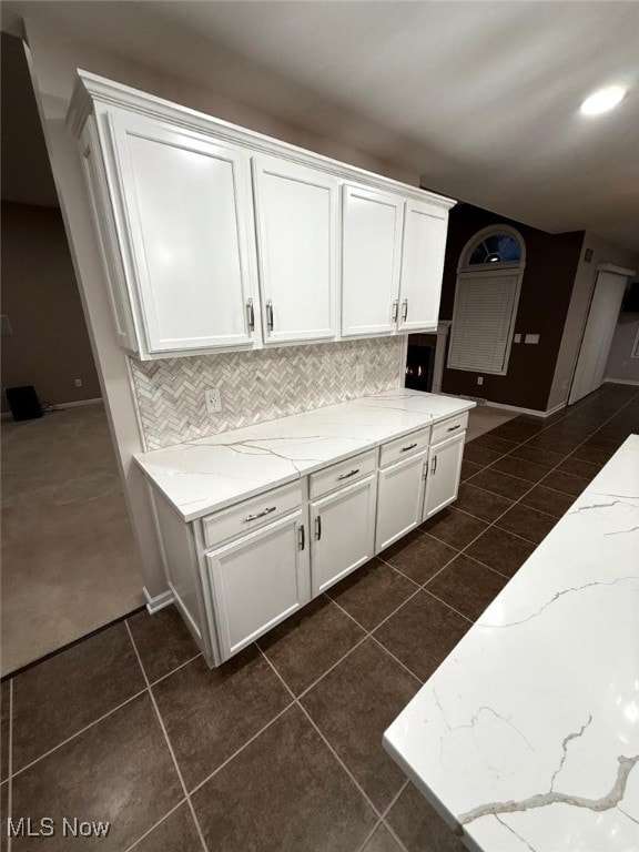 kitchen with dark tile patterned floors, light stone countertops, and white cabinetry