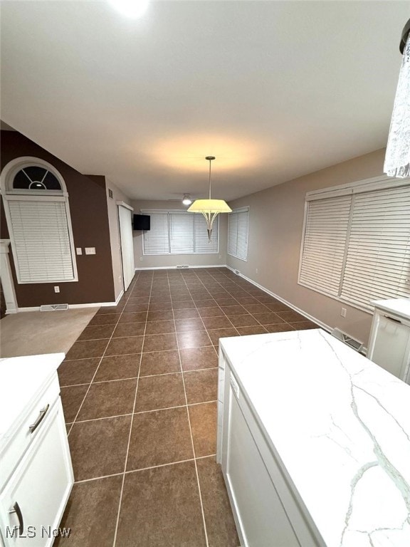 interior space featuring white cabinets, light stone countertops, dark tile patterned floors, and hanging light fixtures