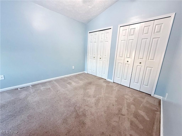 unfurnished bedroom featuring carpet floors, two closets, a textured ceiling, and vaulted ceiling