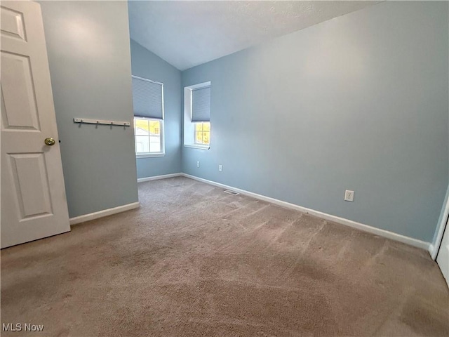 spare room featuring light carpet and vaulted ceiling