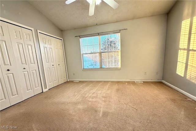 unfurnished bedroom with ceiling fan, multiple closets, lofted ceiling, a textured ceiling, and carpet flooring