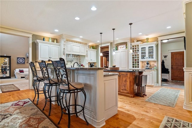 kitchen featuring a center island with sink, a kitchen breakfast bar, white cabinets, hanging light fixtures, and tasteful backsplash