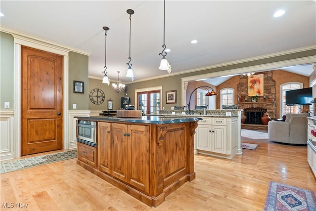 kitchen with dark stone counters, crown molding, decorative light fixtures, a center island with sink, and a fireplace