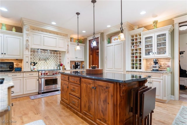 kitchen featuring pendant lighting, designer range, dark stone countertops, tasteful backsplash, and white cabinetry