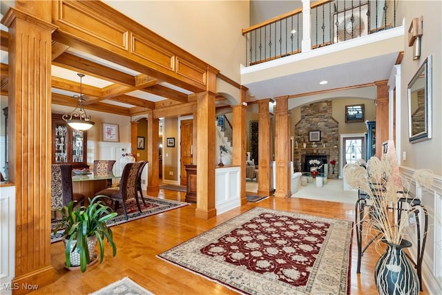 entryway featuring ornate columns, a fireplace, coffered ceiling, beamed ceiling, and light hardwood / wood-style floors