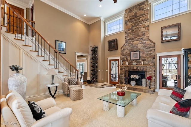 carpeted living room with a towering ceiling, a stone fireplace, and crown molding