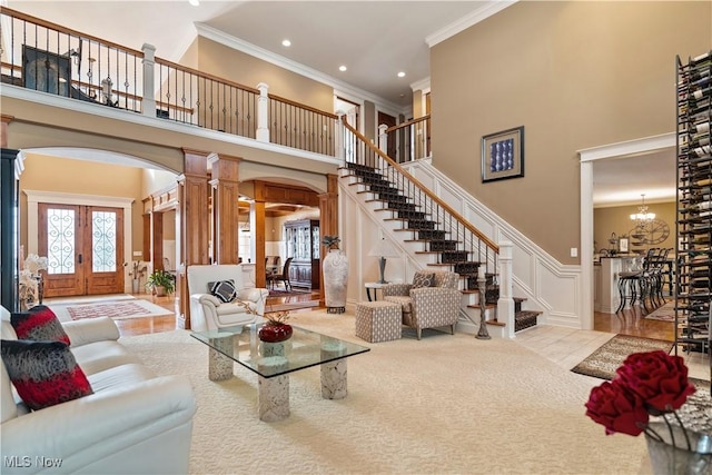 living room with french doors, a high ceiling, decorative columns, crown molding, and a chandelier