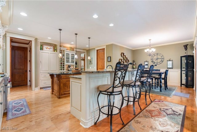 kitchen featuring hanging light fixtures, light stone counters, a kitchen bar, a center island with sink, and ornamental molding