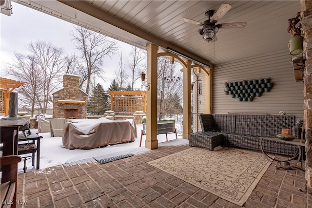 snow covered patio featuring an outdoor stone fireplace and ceiling fan