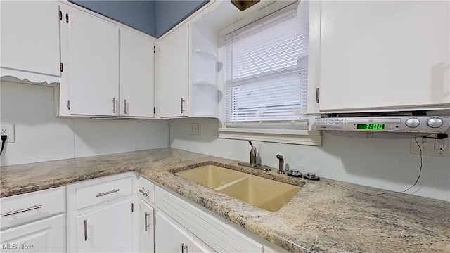 kitchen featuring white cabinets, light stone counters, and sink