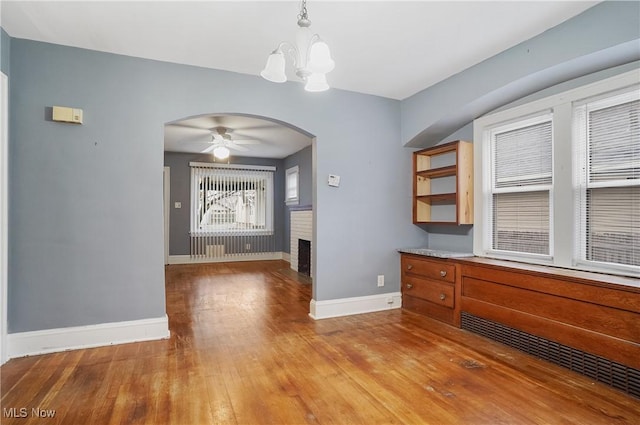 unfurnished dining area with a fireplace, ceiling fan with notable chandelier, and light hardwood / wood-style floors