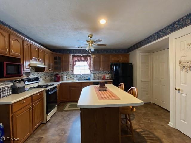 kitchen with a breakfast bar, a center island, black appliances, decorative backsplash, and ceiling fan