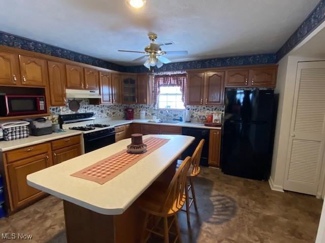 kitchen featuring a kitchen bar, ceiling fan, sink, black appliances, and a center island