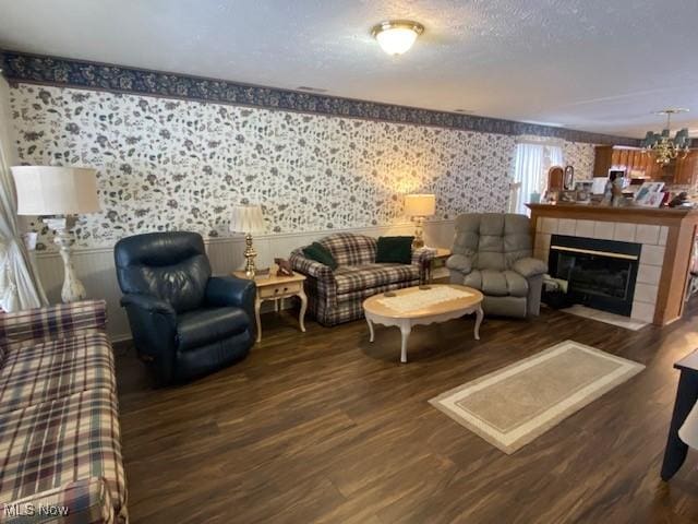 living area featuring dark wood finished floors, an inviting chandelier, a textured ceiling, a tile fireplace, and wallpapered walls