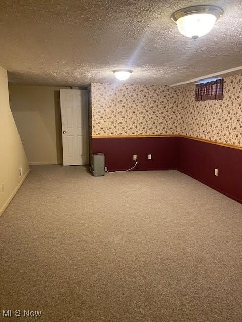 finished below grade area featuring a textured ceiling, carpet, baseboards, and wallpapered walls