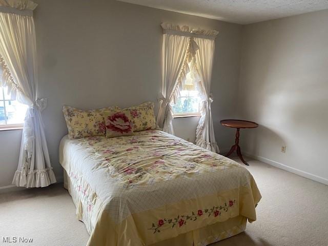 bedroom featuring baseboards, light colored carpet, and a textured ceiling