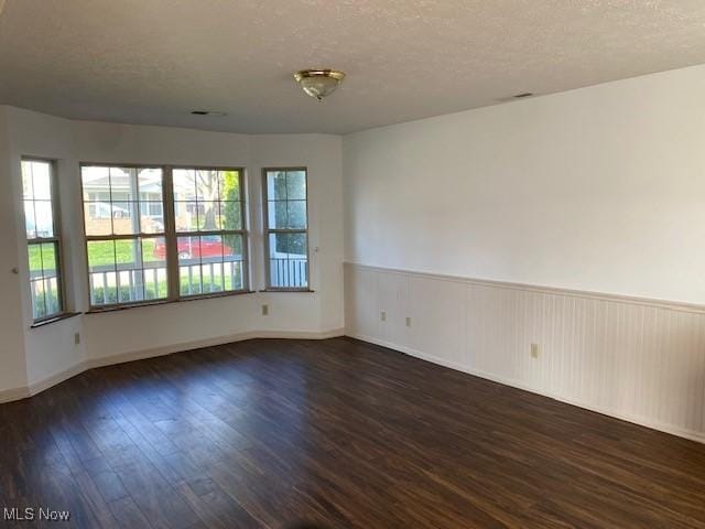 unfurnished room with dark wood-style flooring, wainscoting, and a textured ceiling