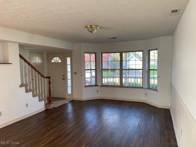 entrance foyer featuring a textured ceiling, wood finished floors, visible vents, and stairway
