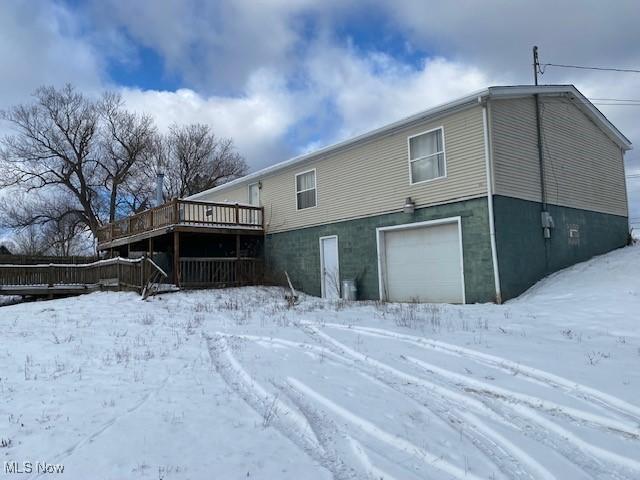 snow covered back of property featuring a deck and a garage