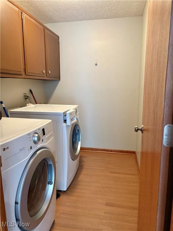 washroom with cabinets, independent washer and dryer, a textured ceiling, and light hardwood / wood-style flooring