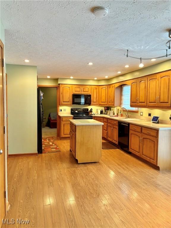 kitchen featuring a textured ceiling, sink, black appliances, a center island, and light hardwood / wood-style floors