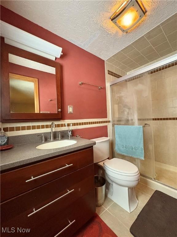 bathroom featuring a textured ceiling, vanity, a shower with door, tile patterned flooring, and toilet