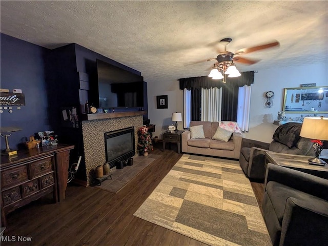 living room with a fireplace, ceiling fan, dark hardwood / wood-style flooring, and a textured ceiling