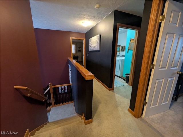 hall with separate washer and dryer, a textured ceiling, and light carpet