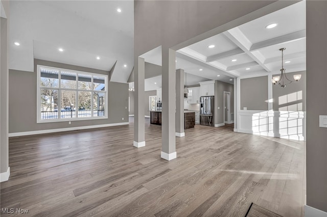 unfurnished living room featuring beamed ceiling, light hardwood / wood-style floors, an inviting chandelier, and coffered ceiling