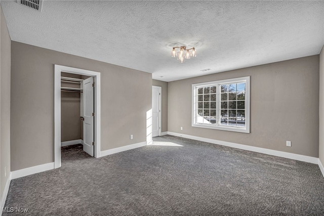 unfurnished bedroom with a walk in closet, a textured ceiling, dark colored carpet, a chandelier, and a closet