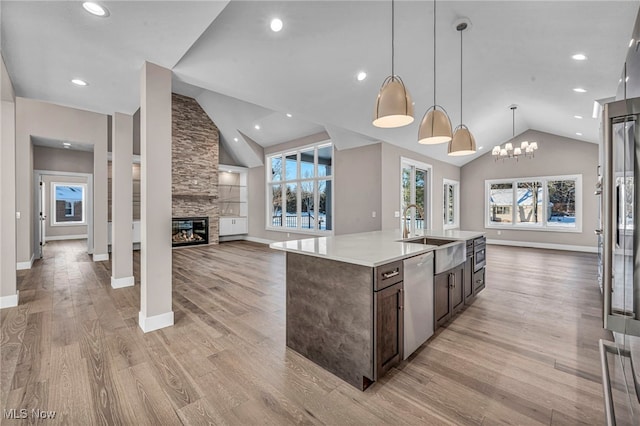 kitchen with stainless steel dishwasher, vaulted ceiling, sink, decorative light fixtures, and an island with sink