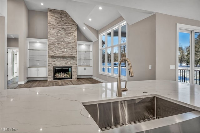 kitchen featuring built in shelves, light stone countertops, sink, high vaulted ceiling, and a fireplace