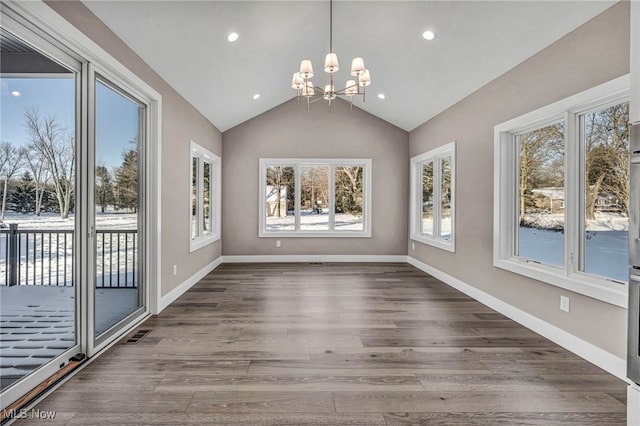 unfurnished dining area featuring hardwood / wood-style flooring, a healthy amount of sunlight, vaulted ceiling, and an inviting chandelier