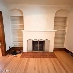 unfurnished living room featuring hardwood / wood-style flooring, built in shelves, and a tiled fireplace