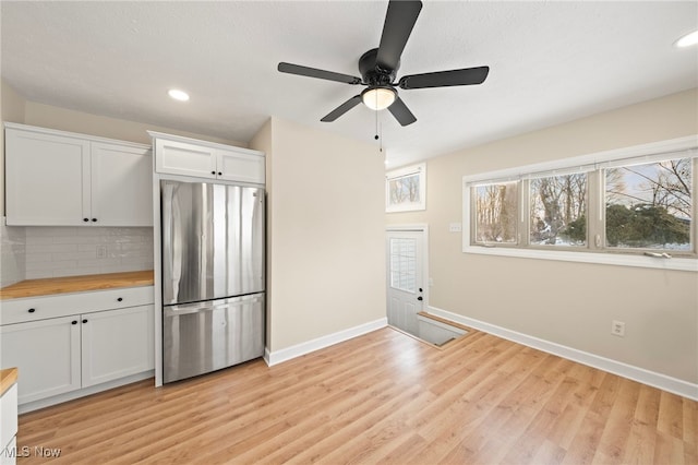 kitchen with decorative backsplash, light wood-type flooring, butcher block counters, white cabinetry, and stainless steel refrigerator