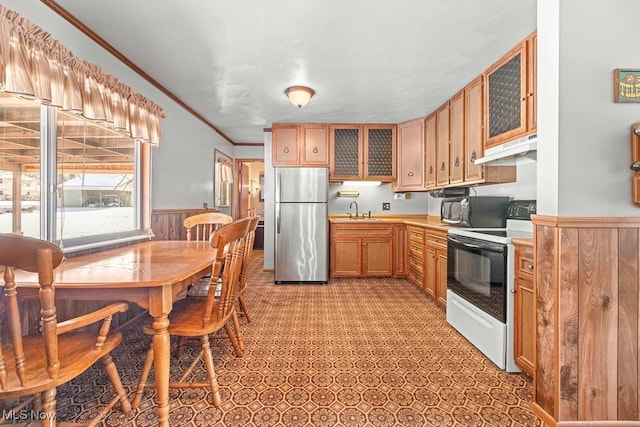 kitchen with stainless steel appliances, crown molding, wood walls, and sink