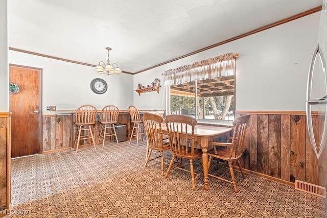 dining room featuring ornamental molding, a notable chandelier, and wooden walls