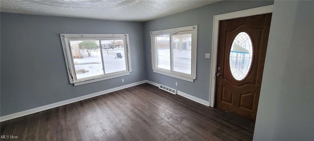 foyer entrance with a textured ceiling, baseboards, dark wood finished floors, and visible vents