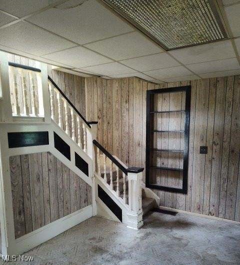 basement featuring a drop ceiling and wood walls