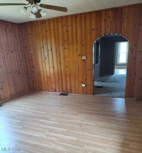 unfurnished room with light hardwood / wood-style flooring, ceiling fan, and wood walls