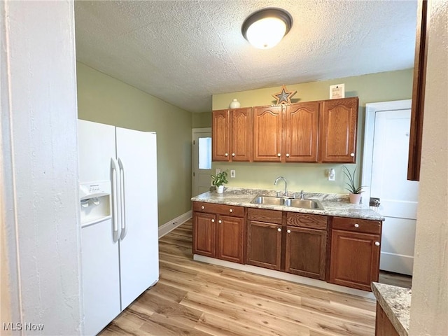 kitchen with light wood-type flooring, light stone counters, a textured ceiling, sink, and white fridge with ice dispenser