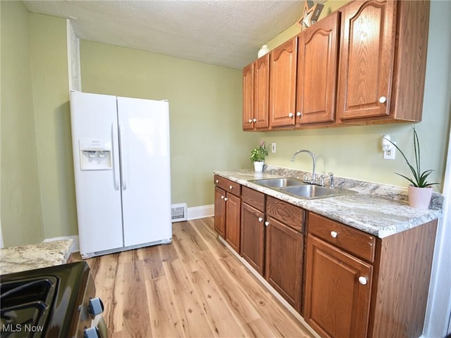 kitchen with stove, sink, light wood-type flooring, a textured ceiling, and white fridge with ice dispenser