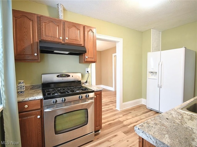 kitchen featuring gas range, light stone countertops, white fridge with ice dispenser, light hardwood / wood-style floors, and a textured ceiling