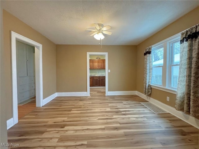 unfurnished dining area with a textured ceiling, light hardwood / wood-style flooring, and ceiling fan